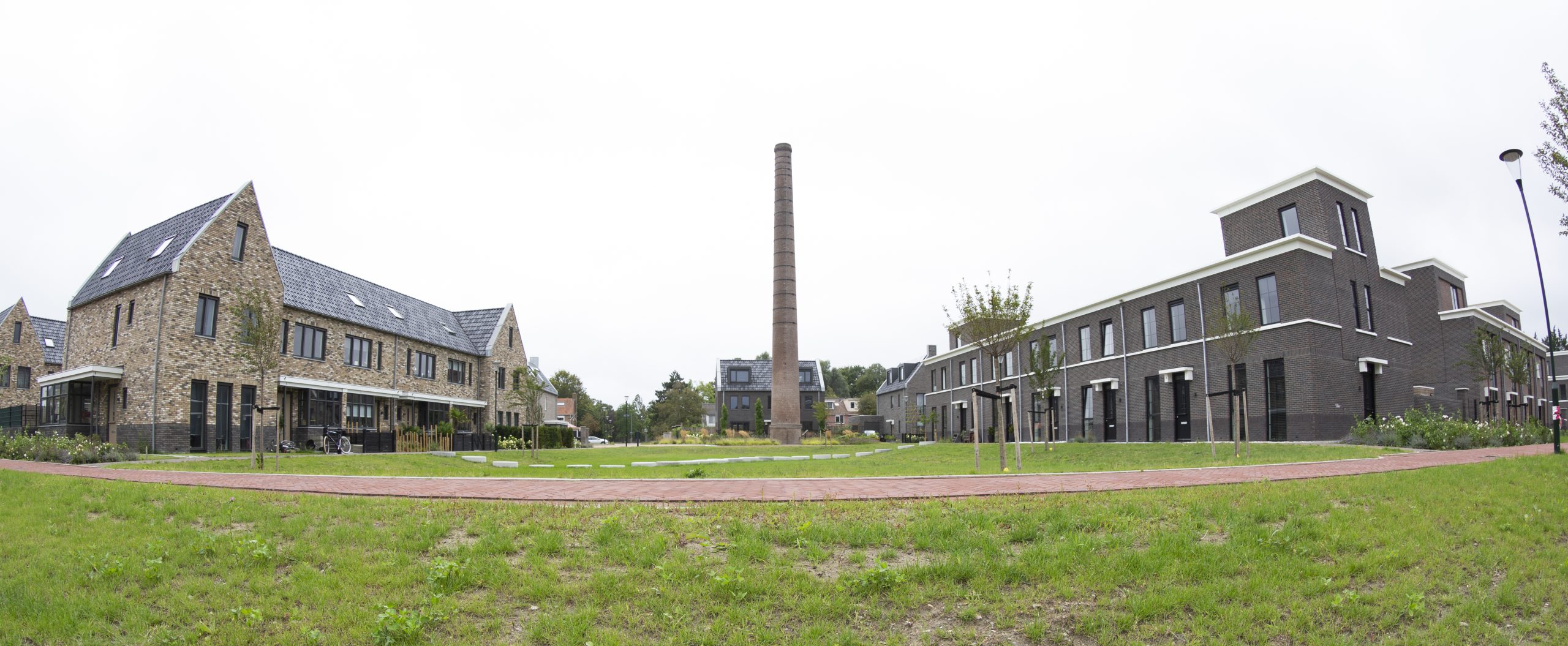 Dit is een afbeelding van het Melco-project in Heiloo: een nieuwe woonwijk gerealiseerd op het terrein van de voormalige melkfabriek (Melkunie/Vampina), met herkenbare elementen zoals de monumentale schoorsteen en architectuur die refereert aan het industriële verleden.