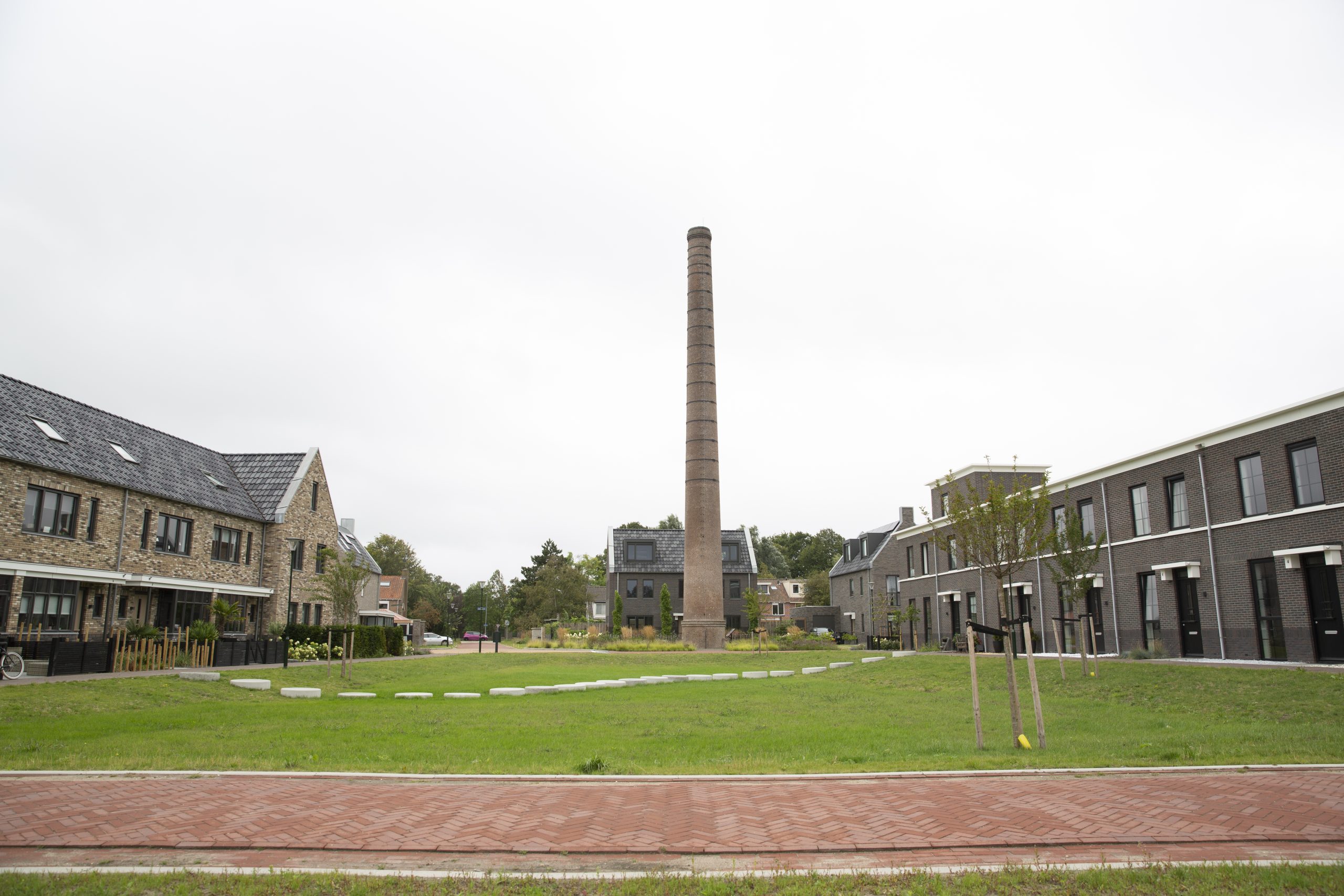 Dit is een afbeelding van het Melco-project in Heiloo: een nieuwe woonwijk gerealiseerd op het terrein van de voormalige melkfabriek (Melkunie/Vampina), met herkenbare elementen zoals de monumentale schoorsteen en architectuur die refereert aan het industriële verleden.